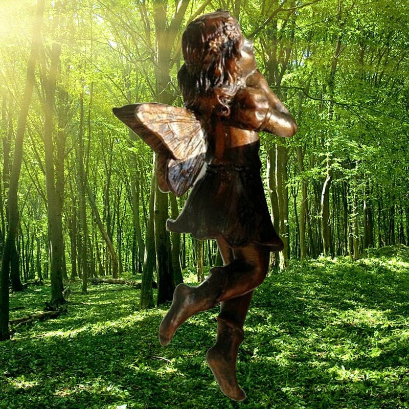 Standing fairy ornament shown against a woodland background, with folded arms, curled hair and warm metallic-tone wings.