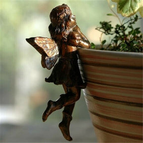 The standing fairy hangs outside a plant pot with its arms folded and one knee bent, shown beside trailing greenery.