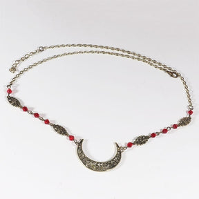 Bronze-tone ornate crescent head chain with small red faceted beads, arranged in an oval on a pale background with the clasp and chain visible.