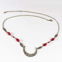 Bronze-tone ornate crescent headdress with large red teardrop beads, arranged in an oval on a pale background with the clasp and chain visible.