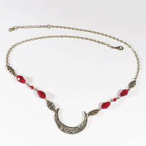 Bronze-tone ornate crescent headdress with large red teardrop beads, arranged in an oval on a pale background with the clasp and chain visible.