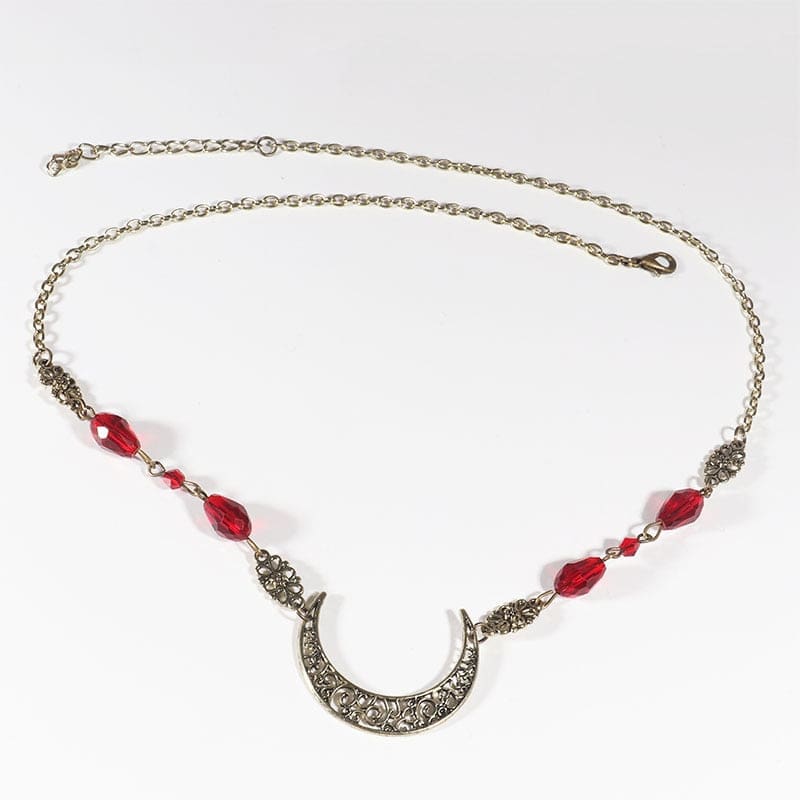 Bronze-tone ornate crescent headdress with large red teardrop beads, arranged in an oval on a pale background with the clasp and chain visible.