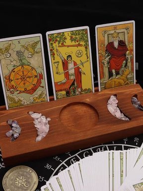 Brown wooden moon phase tarot stand displaying three illustrated cards, with small stones in the crescent recesses and a fanned deck below.