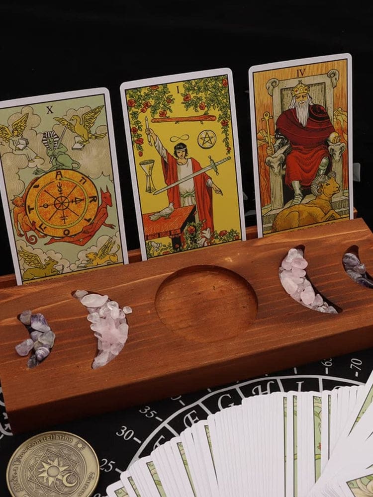 Brown wooden moon phase tarot stand displaying three illustrated cards, with small stones in the crescent recesses and a fanned deck below.