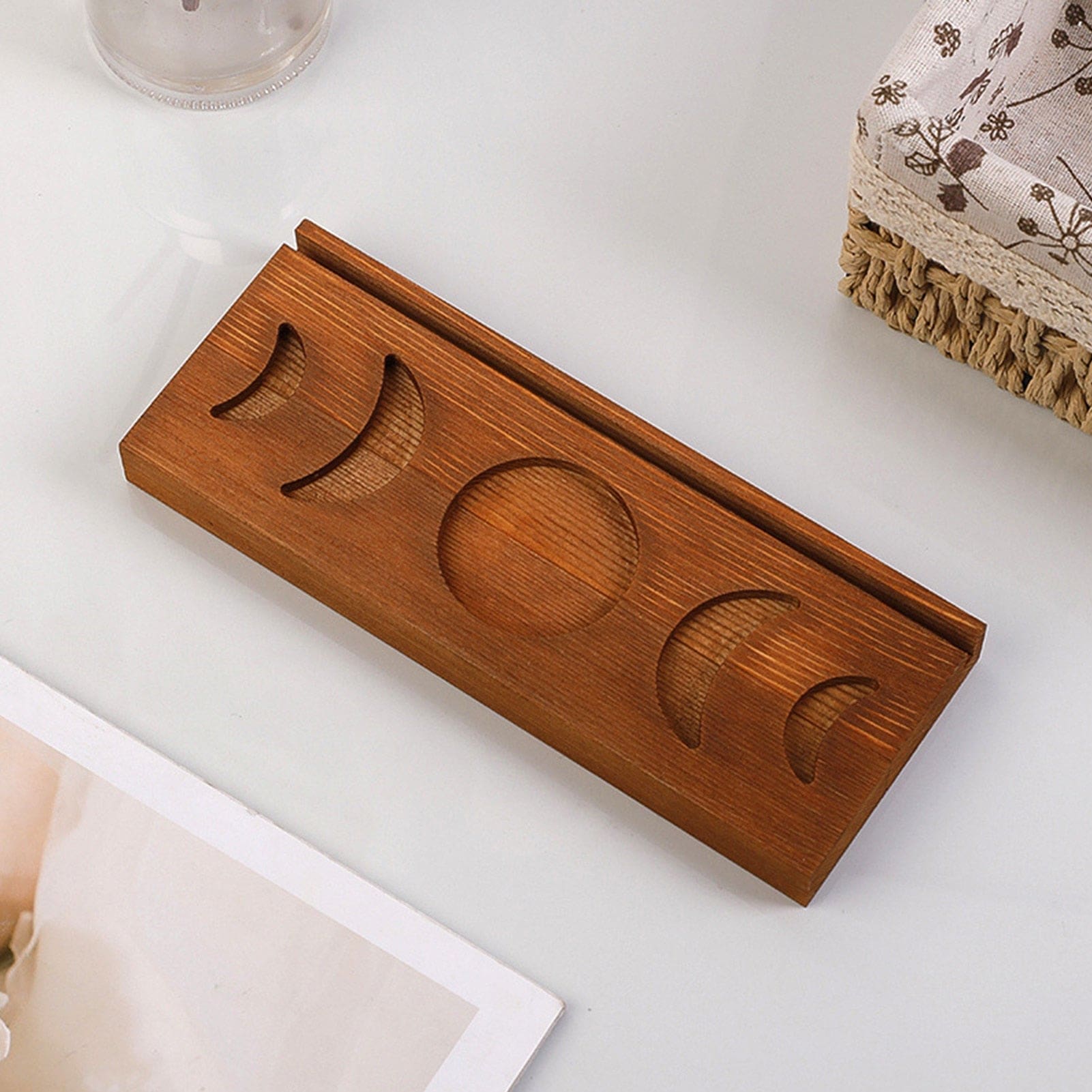 Overhead view of the empty brown moon phase tarot stand on a white surface beside fringed fabric, showing all five moon recesses.