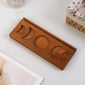 Overhead view of the empty brown moon phase tarot stand on a white surface beside fringed fabric, showing all five moon recesses.