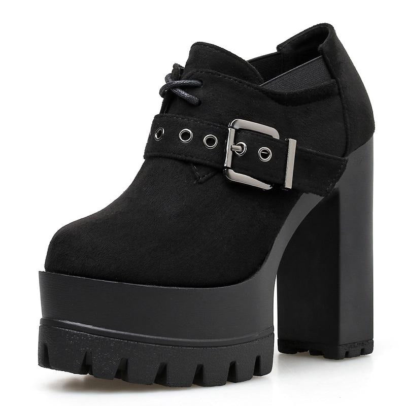 Close angled view of a black platform ankle bootie, highlighting the large silver-tone buckle, eyelet strap and notched forefoot sole.
