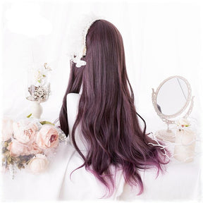 Back view of the burgundy wig showing loose waves through its long lengths. The wig is displayed on a white mannequin beside pale flowers and an ornate mirror.