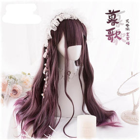 Angled front view of the dark burgundy wig styled with a narrow braid and white lace headpiece. A mirror, flowers and a candle decorate the pale display; supplier lettering overlays the photo.