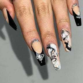 Black French-tip coffin nails with white butterfly outlines, marbled black-and-white swirls and small gem-like accents near the cuticles.