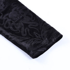 Black velvet trouser cuff viewed at an angle, with curled botanical motifs and a narrow stitched edge.