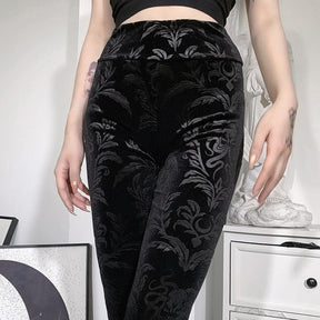 Front close-up of the black patterned velvet pants, showing curling leaf shapes and serpentine flourishes through the hips and thighs.