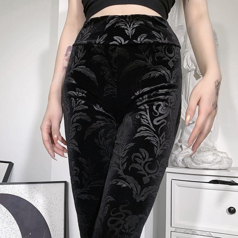 Front close-up of the black patterned velvet pants, showing curling leaf shapes and serpentine flourishes through the hips and thighs.