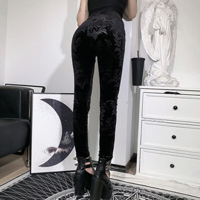 Rear styling view of the high-waisted black velvet pants, with fitted legs extending to strappy black shoes.