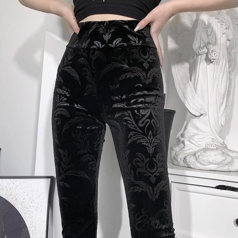 Close-up of the high waistband and front botanical scrollwork on the black velvet pants, shown with hands at the hips.