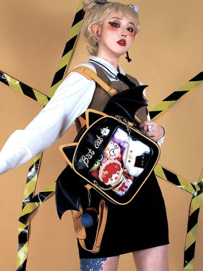 Side outfit view of the black and golden-orange cat backpack, with broad bat wings and character collectibles behind the clear display panel.