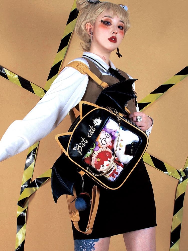 Side outfit view of the black and golden-orange cat backpack, with broad bat wings and character collectibles behind the clear display panel.
