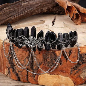 Black triple-moon crystal crown displayed on a wood slice with its chains draped in front.