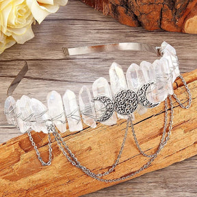 Clear crystal-point triple-moon crown resting on wood beside pale flowers.