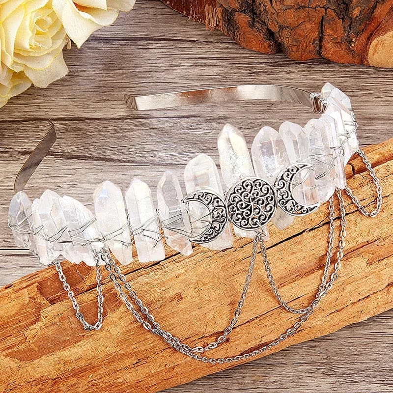 Clear crystal-point triple-moon crown resting on wood beside pale flowers.
