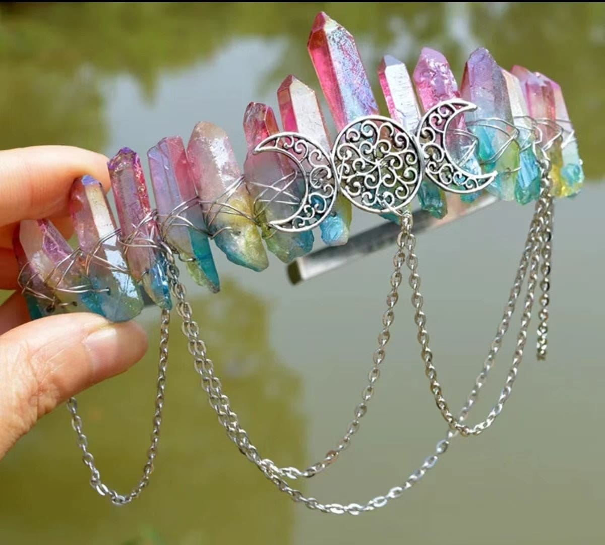 Pink-to-blue crystal crown held outdoors, showing the triple moon motif and chain drapes.