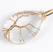 Clear quartz pendant with gold-tone tree branches and a twisted trunk visible through the pale stone.