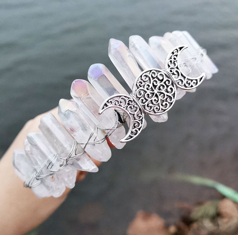 Angled view of a clear crystal point crown with a silver-tone triple moon emblem and wire-wrapped band.