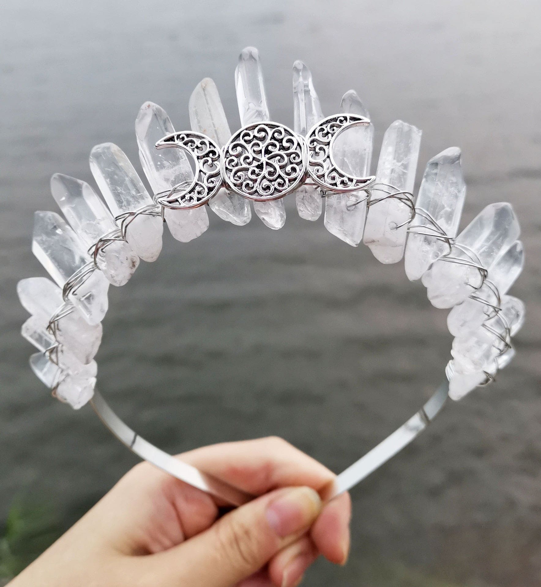 Pale clear crystal points rise in an uneven row above an ornate silver-tone triple moon motif on the crown.