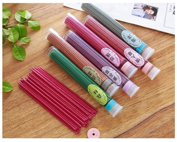 Clear fragrance tubes and loose pink incense sticks arranged on wood, with a small round holder beside the sticks.