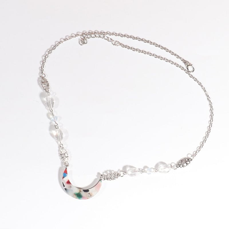 Silver-tone headdress with clear teardrop beads and a pale acrylic crescent scattered with colourful flecks, arranged in an oval on a pale background with the clasp and chain visible.