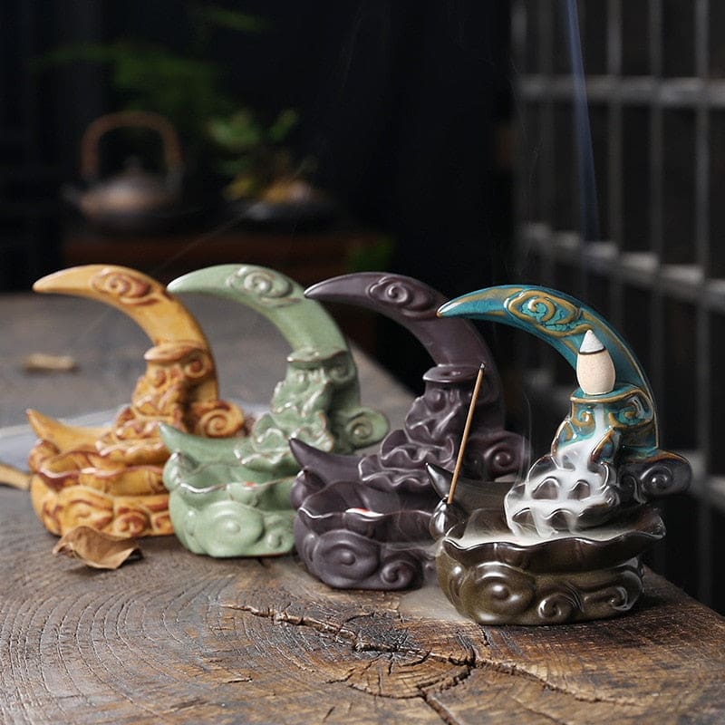 Yellow, Green, Black and Blue crescent moon incense burners arranged together on rustic wood, showing the four colour options and their curved sculpted bases.