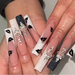 Another view of the long crown-charm nail set, showing glittered black-and-white tips, lip artwork and raised silver-tone embellishments.