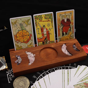 Square view of the brown tarot stand supporting three cards, with pale and dark crystal chips arranged in the recessed crescent shapes.