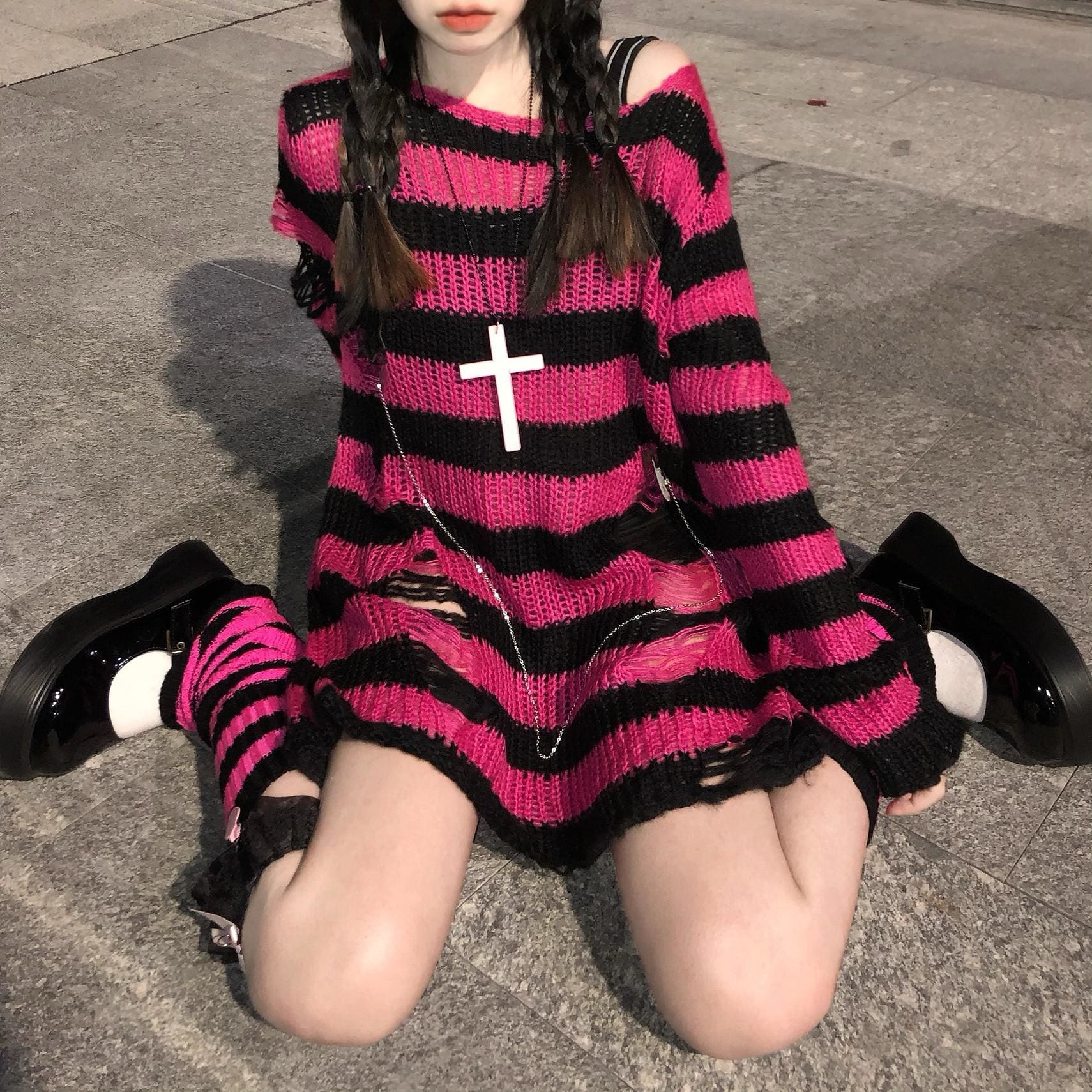 Fuchsia and black striped long sweater worn on a staircase, showing a wide neckline and distressed lower front. It is styled with striped socks and dark accessories.