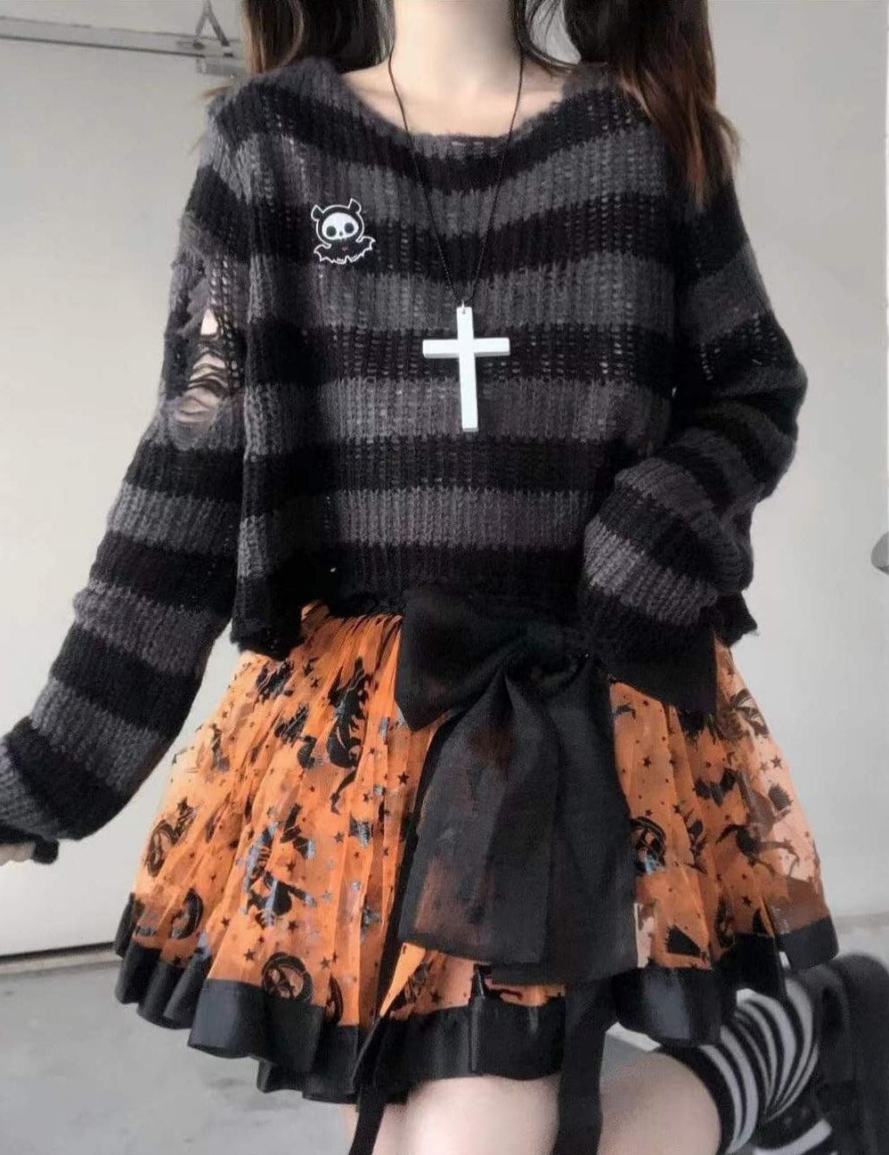 Grey and black distressed cropped sweater worn with an orange-and-black skirt and a large black waist bow. The loose neckline, long sleeves and torn upper sleeve are visible.