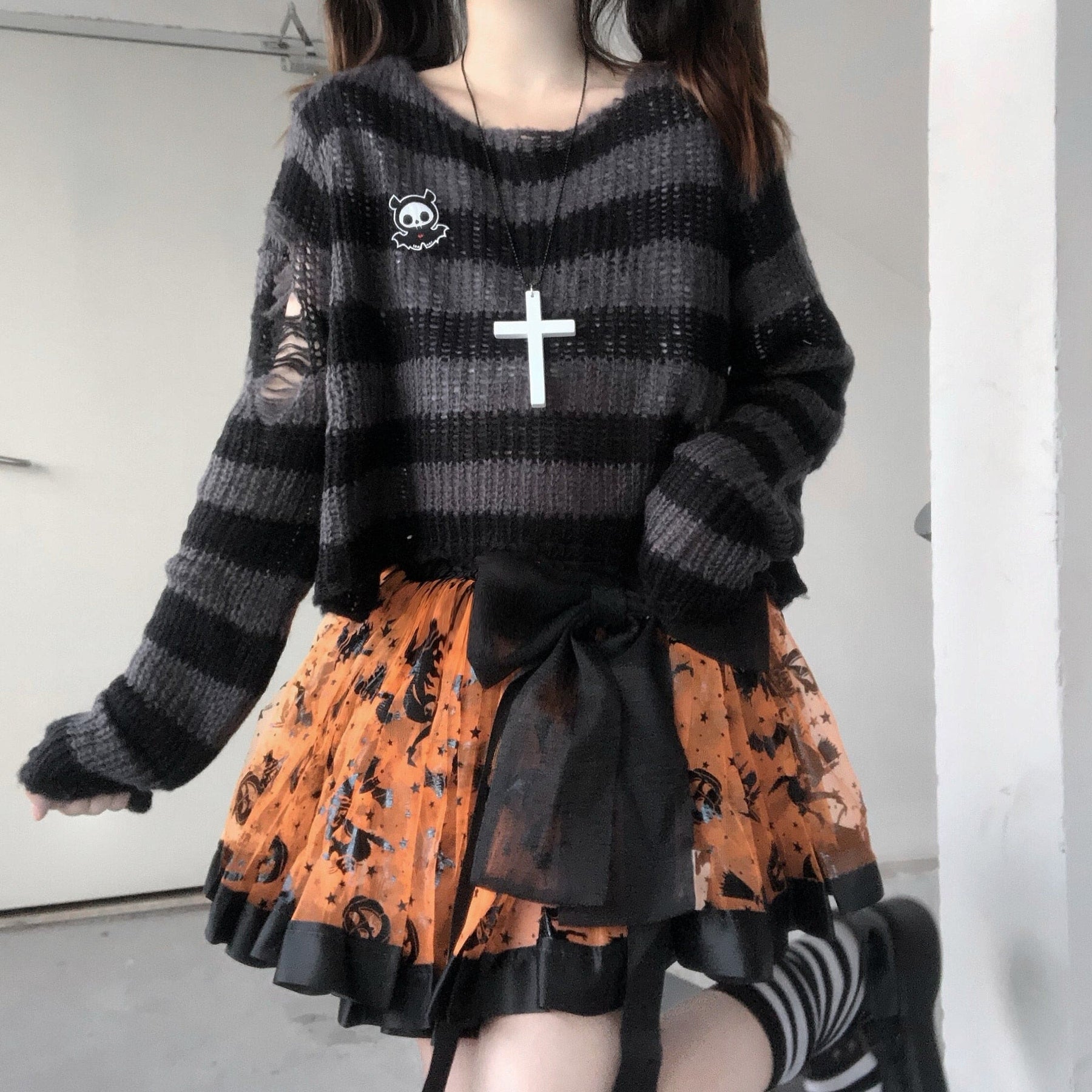 Grey and black cropped striped sweater shown from the neckline to the orange skirt below. Loose sleeves and torn sections contrast with the structured waist bow.