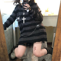 Long grey and black distressed striped sweater shown in a kneeling mirror photo, styled with a chain, cross necklace and black skirt underneath.