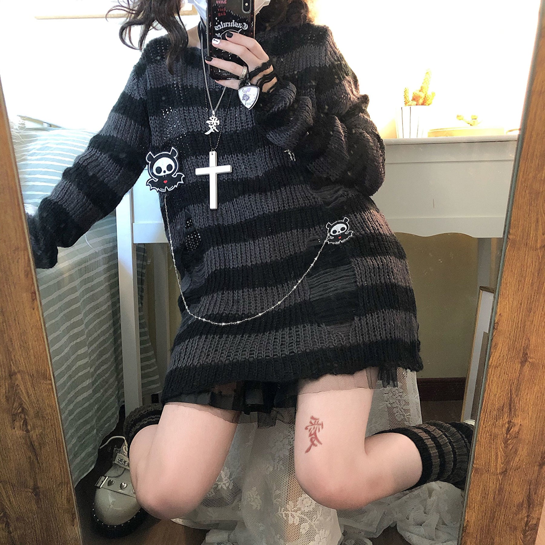 Grey and black long striped sweater in a closer mirror view, with a chain draped across the lower front and a black skirt peeking below the hem.
