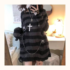 Standing front mirror view of a long grey and black striped sweater with a black skirt underneath. Silver-tone necklaces and a waist chain are styled over the knit.