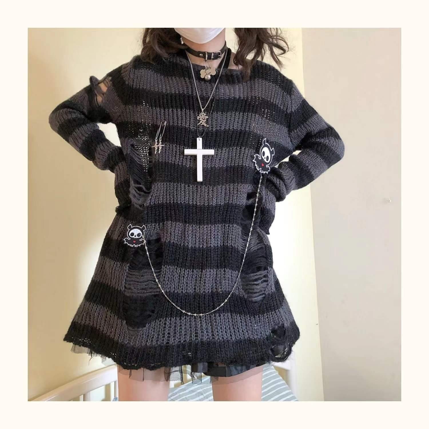 Grey and black long striped sweater worn with hands at the waist. Distressed side openings, a loose hem and a chain across the front are visible.
