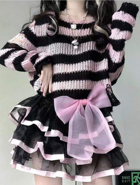 Pink and black striped cropped knit sweater worn with a black ruffled skirt, pink trim and a large pale pink bow. The model lifts one arm beside the staircase.