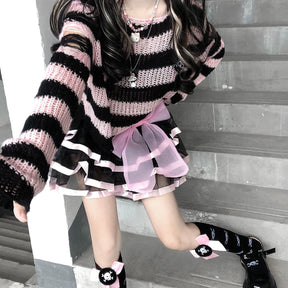 Pink and black cropped sweater seen from above on a staircase, styled with a pink-trimmed skirt, black socks and shoes. The model extends an arm toward the camera.