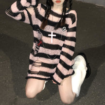 Long pink and black striped sweater worn on a staircase, with laddered openings near the lower side and long sleeves. A skull pin and necklace are styled on the front.