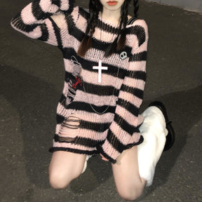 Long pink and black striped sweater worn on a staircase, with laddered openings near the lower side and long sleeves. A skull pin and necklace are styled on the front.