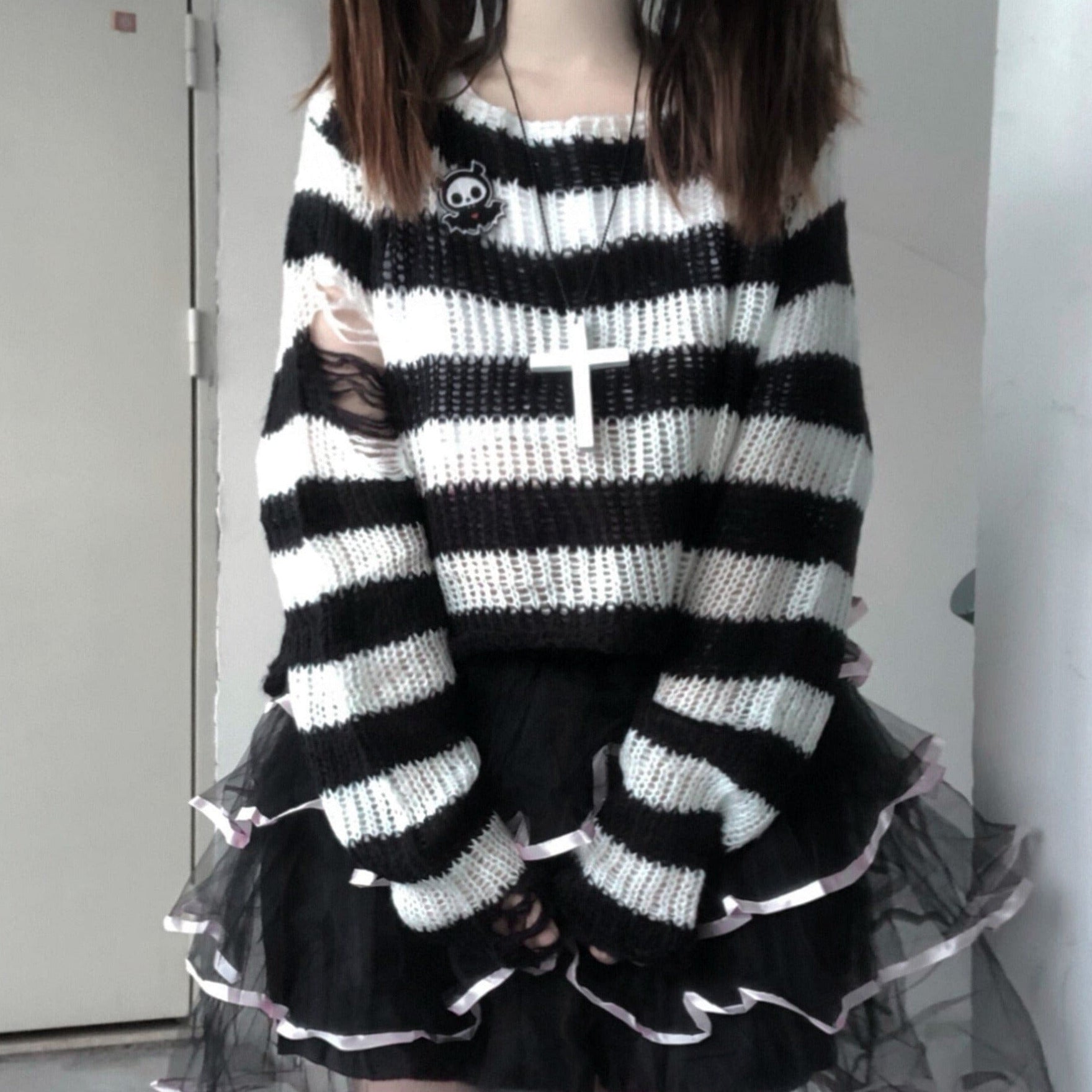 White and black striped slouchy sweater worn over a layered black skirt with white ribbon trim. A wide neckline and distressed sleeve openings add grunge detail.