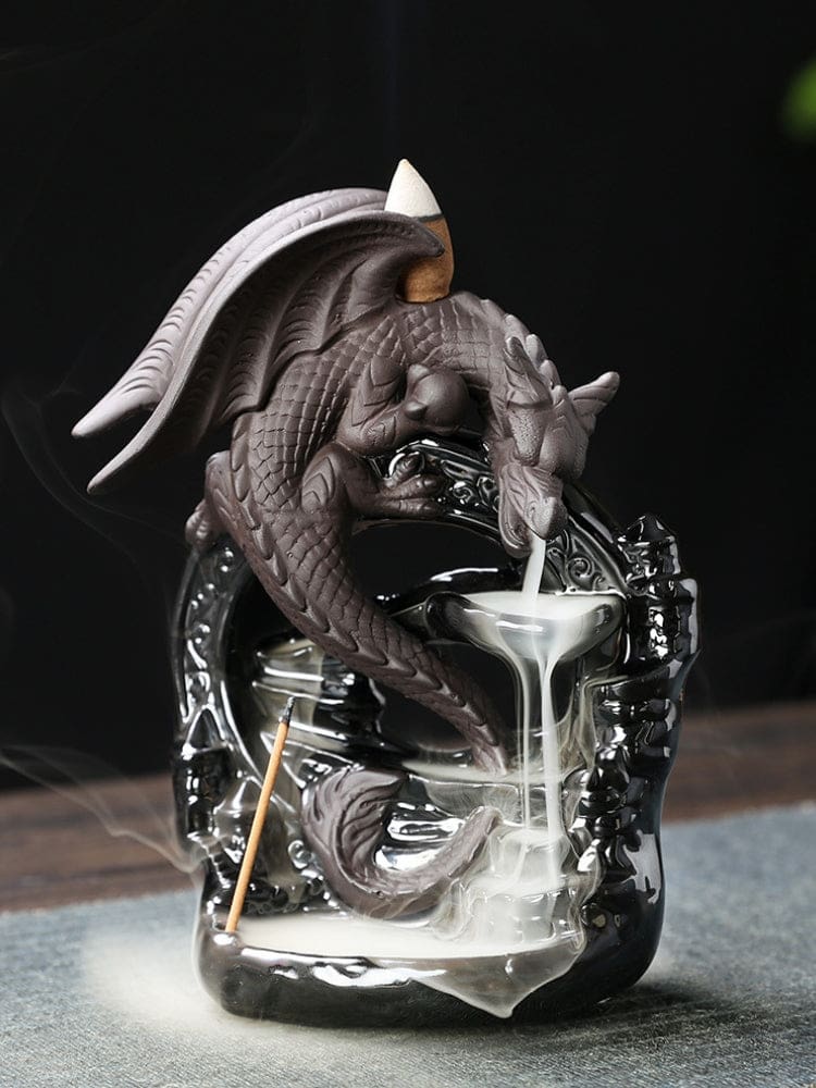 Gray dragon backflow incense burner breathing smoke into tiered bowls on a glossy black arch-shaped base, with mist pooling below its curled tail.