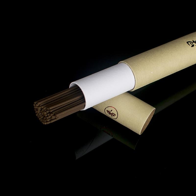 Close view of an open paper incense tube with slender brown sticks extending from its white inner sleeve.