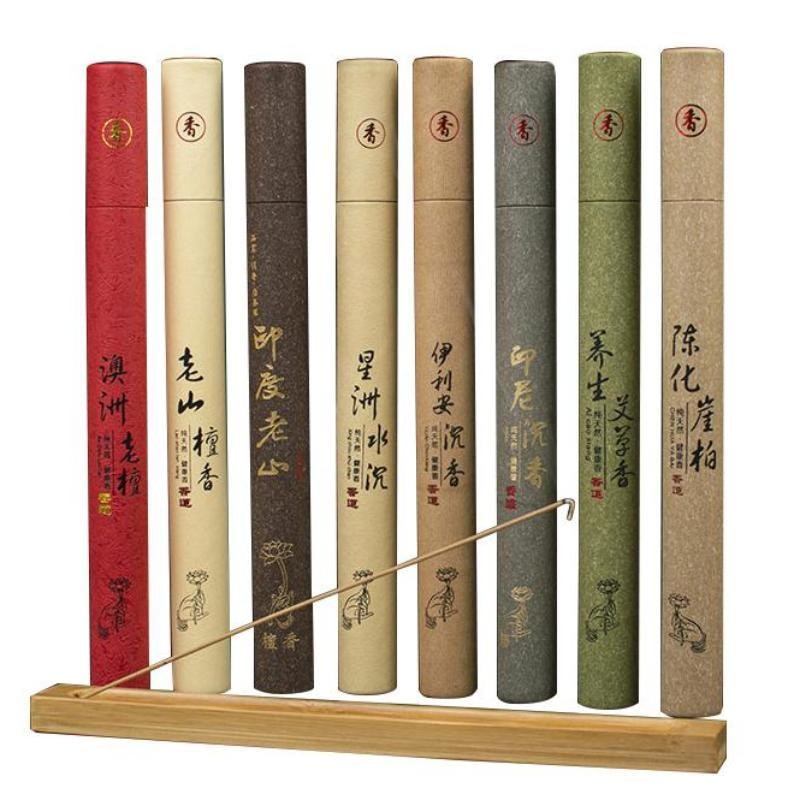Tall paper tubes of earthy and woody incense in red, green and neutral colours, displayed with a wooden stick holder on a white background.