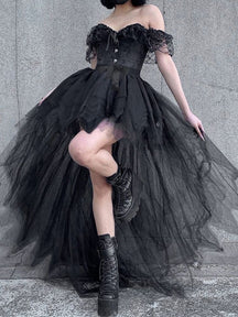 Black fairy grunge tutu skirt on a model posing with one knee raised beside a gray wall, showing the layered hem over fishnet tights.