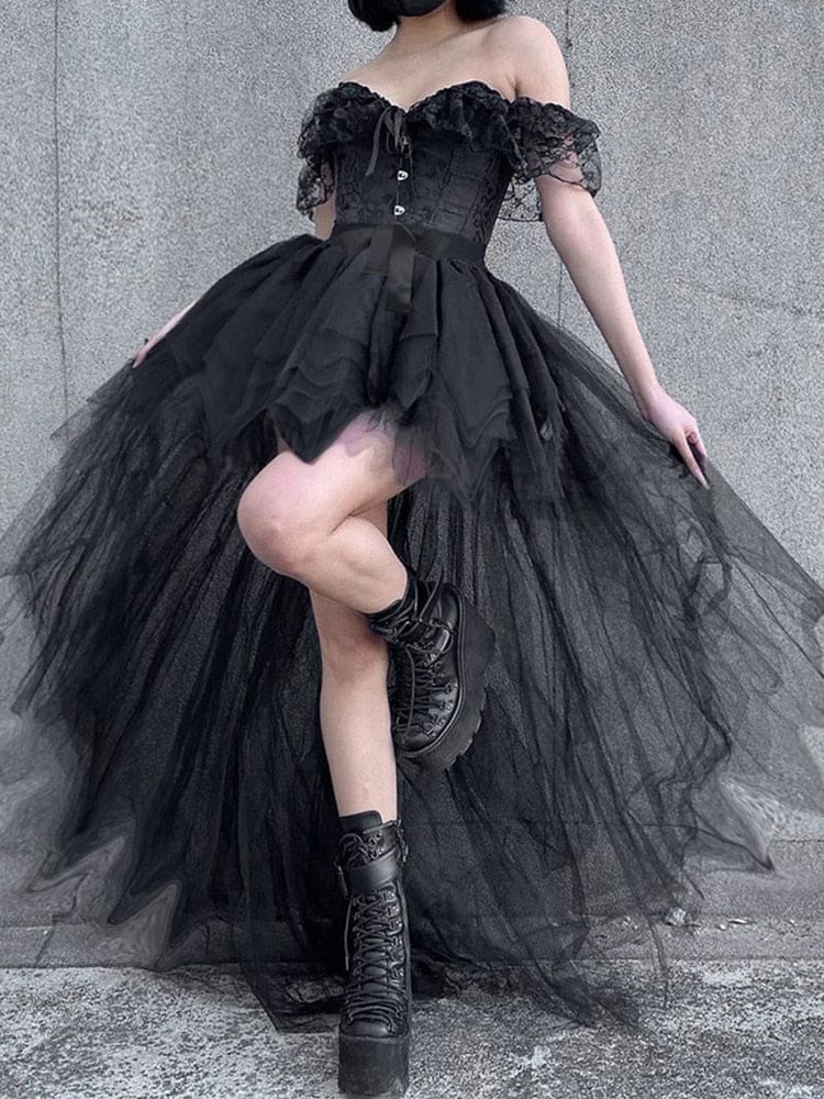 Black fairy grunge tutu skirt on a model posing with one knee raised beside a gray wall, showing the layered hem over fishnet tights.